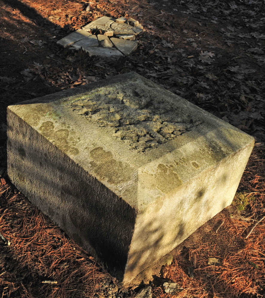 A cracked tombstone on the ground and the base of a four-sided obelisk are in the Edgecomb cemetery in Gardiner.