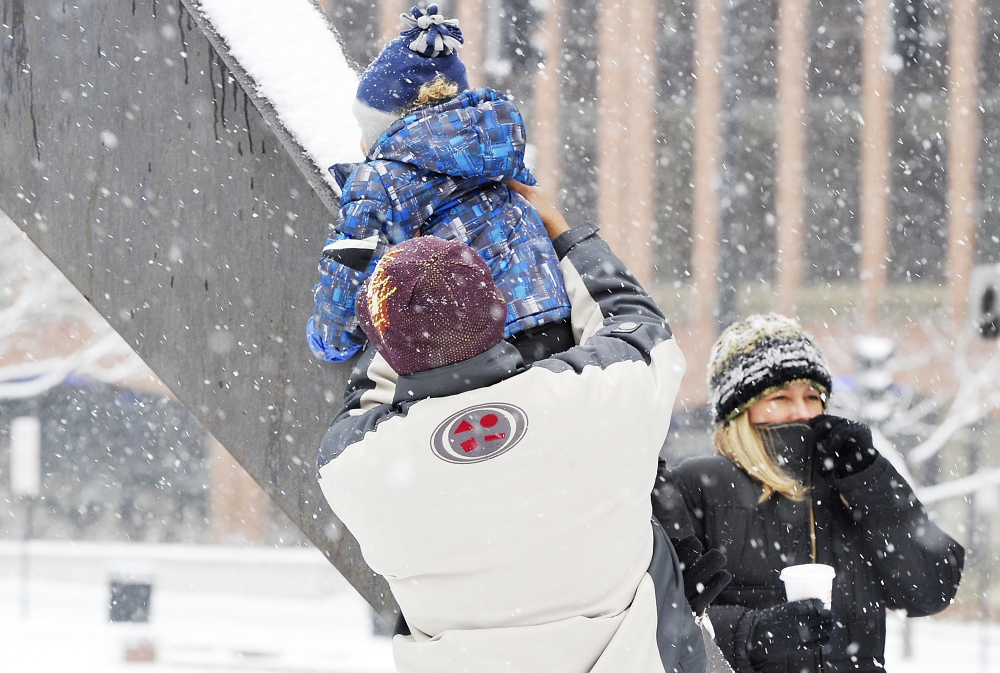 Snow falls as Lenny Medina helps his son, Odalis, slide on a metal sculpture in City Center Plaza on Saturday while Anna Medina, right, bundles up in the stormy weather.