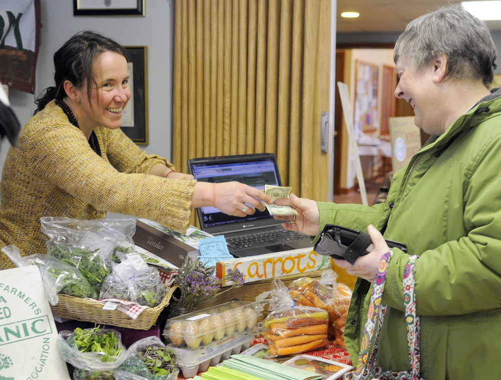 Dalziel Lewis makes change for Kathy Kellison, of Windsor, after she purchased eggs and produce from Lewis’ community supported agricultural business, Dig Deep Farm, during an exhibition for farmers in Hallowell on Sunday.