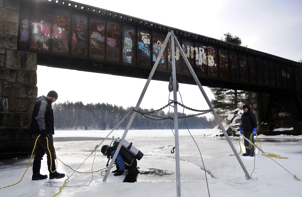 Matt Sinclair dives under the ice on Maranacook Lake in Winthrop tethered by Ben Sniffen, left, and his father, David, on Sunday. The trio from Sea Venture Charters of Wayne recovered a snowmobile that fell through the ice. Matt Sinclair secured a rope around the sled on his first dive.