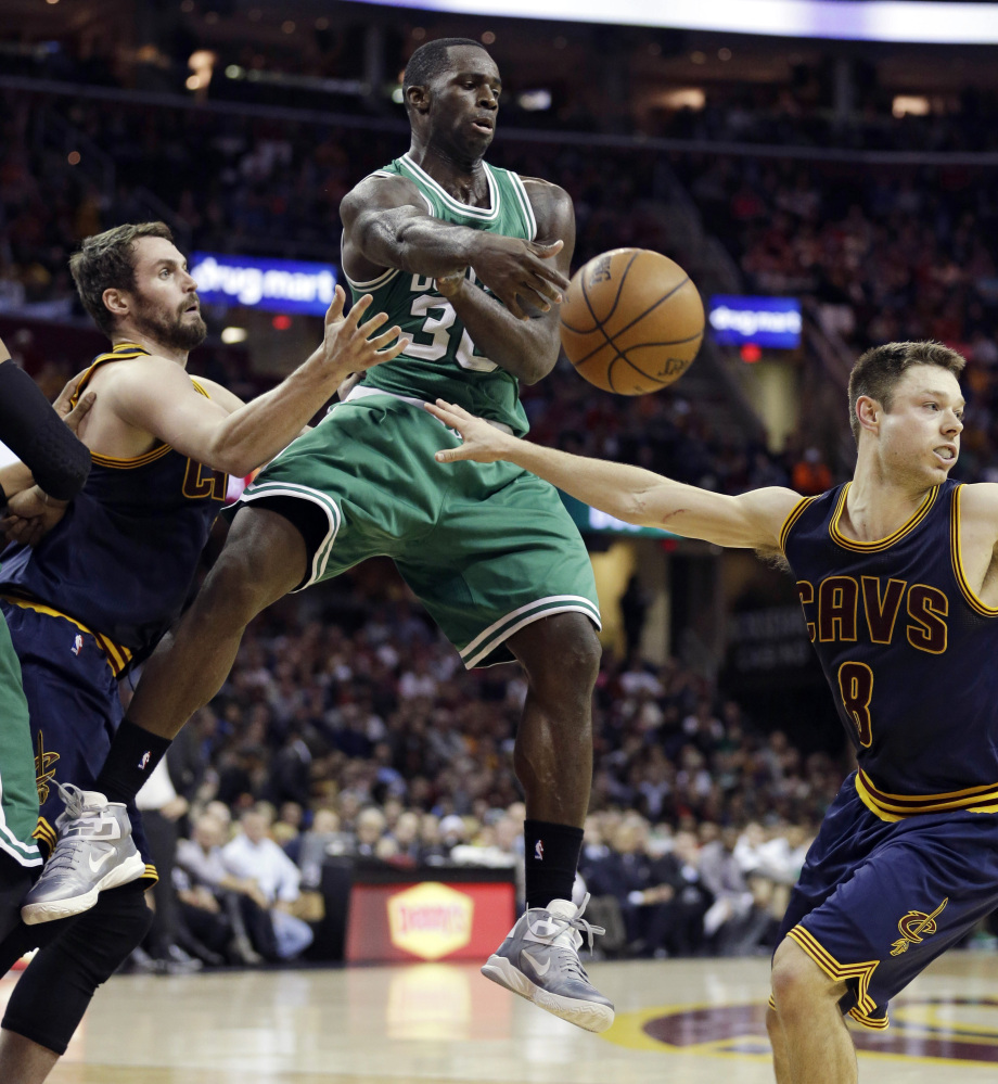 Boston Celtic Brandon Bass passes around the Cavaliers’ Kevin Love, left, and Matthew Dellavedova during the during the second quarter Friday night in Cleveland.