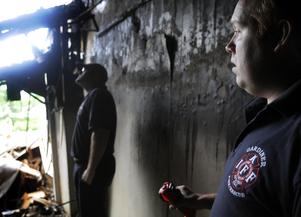 Gardiner firefighter Gary Hickey, left, and fire Capt. Nate Sutherberg wait Sunday in a doorway for colleagues to search the burned-out shell of 235 Water St. for missing equipment. The crew hoped to recover gear lost in the blaze that destroyed the structure last Thursday.