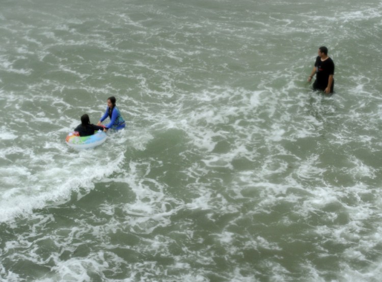 Chris Caiazzo of Hudson, N.H., keeps watch on his sisters Allie, 9, left, and Sarah, 10, of Pepperell, Mass., as they play in the surf near the Old Orchard Beach Pier on Tuesday. Chris said the current didn’t seem too strong. The family wanted to make the best of their vacation and decided to swim despite the heavy rain and wind.