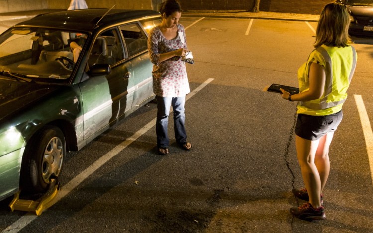 Heather McIntosh, left, prepares to pay Shannon Farrell, a parking enforcement attendant for Unified Parking Partners, to have a boot removed from her car at Post Office Square in this Sept. 10, 2015, photo.