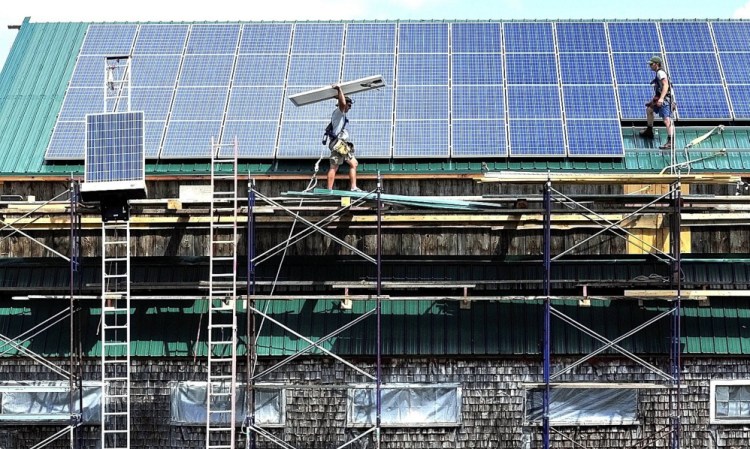 Brian Byrne, left, and Ryan Herz of ReVision Energy install solar panels on a restored Maine Organic Farmers and Gardeners Association barn in Thorndike in 2011.