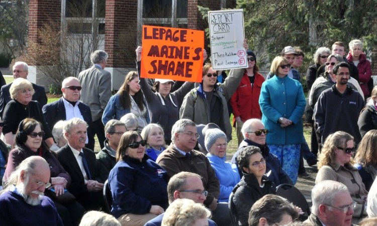 University of Maine in Farmington students Allyson Hammond, left, and Nickolas Bray hold up signs Tuesday criticizing Gov. Paul LePage during the dedication of the Theodora Kalikow Education Center at the school.