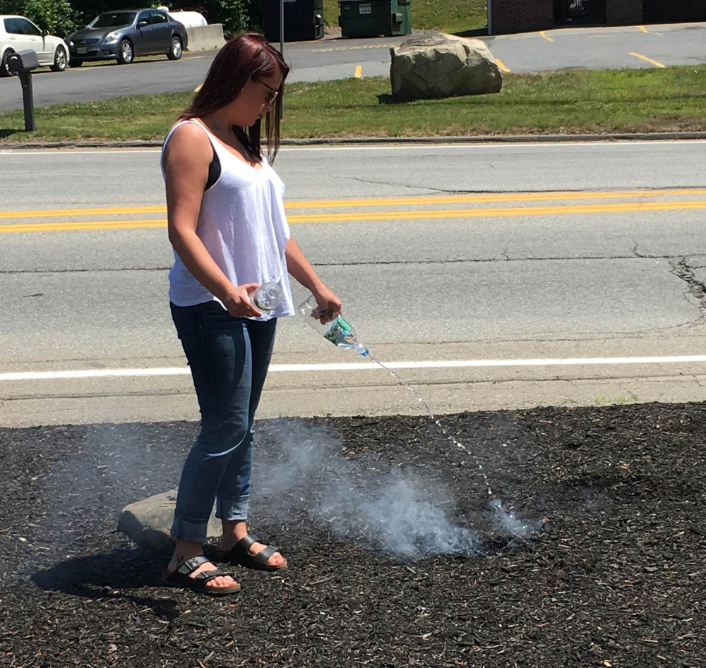 Jordan Genest of Augusta pours water on smoldering bark mulch Friday at a Citgo station in Augusta.