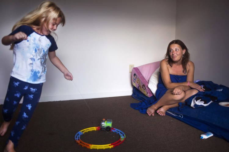 Arianna runs around her room playing with a toy train as Chrissy Chavez sits on Arianna's bed in their apartment. The family is still sleeping on the the same makeshift beds and uses the same camp chairs they used while living in the woods.