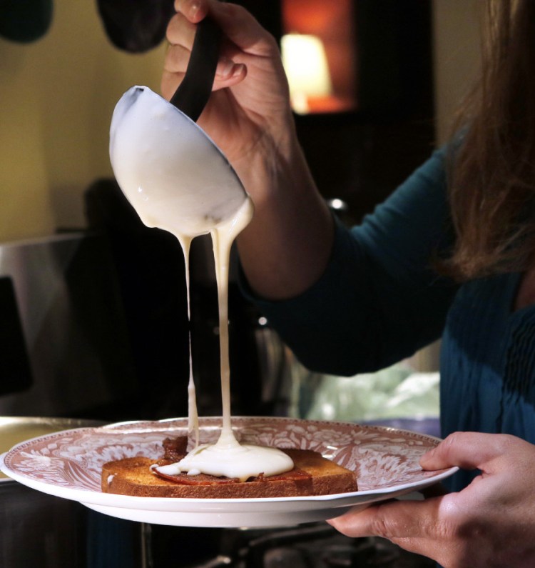 Mollie Martin ladles a cheese sauce over toast topped with bacon in the kitchen of her Kittery Point home. The family favorite originated with her great-grandmother, Queenie Sanders.