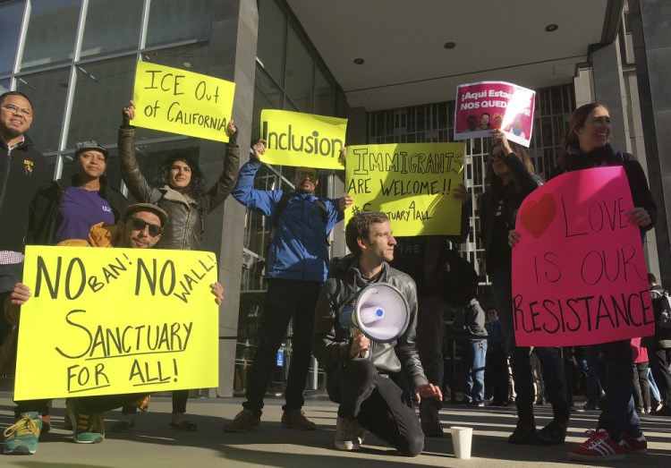 Protesters hold signs outside a courthouse where a federal judge heard arguments in the first lawsuit challenging President Trump's executive order to withhold funding from communities that limit cooperation with immigration authorities on April 14 in San Francisco. U.S. District Court Judge William Orrick held a hearing on San Francisco's request for a court order blocking the Trump administration from cutting off funds to any of the nation's so-called sanctuary cities.