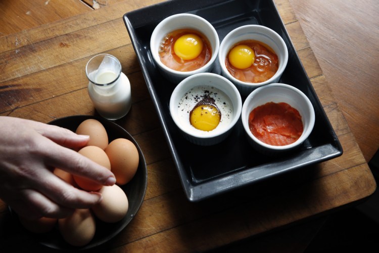 Eggs are cracked into salmon-lined ramekins. Heavy cream, dulse flakes and black pepper are added.