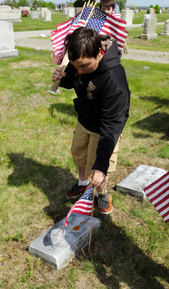 Brody Sanborn places a flag next to a veteran's grave Wednesday in Mount Hope Cemetery in Augusta. Whitefield students helped place flags on veterans' graves in the section near the Augusta State Airport.