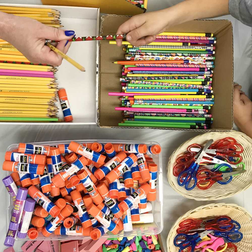 A volunteer, left, hands a pencil to a student during the backpack and school supplies giveaway on Saturday at Augusta Elks Lodge.