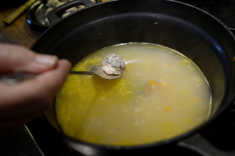 Christine Burns Rudalevige lowers a meatball into broth while cooking a meatball soup with fermented herbs.