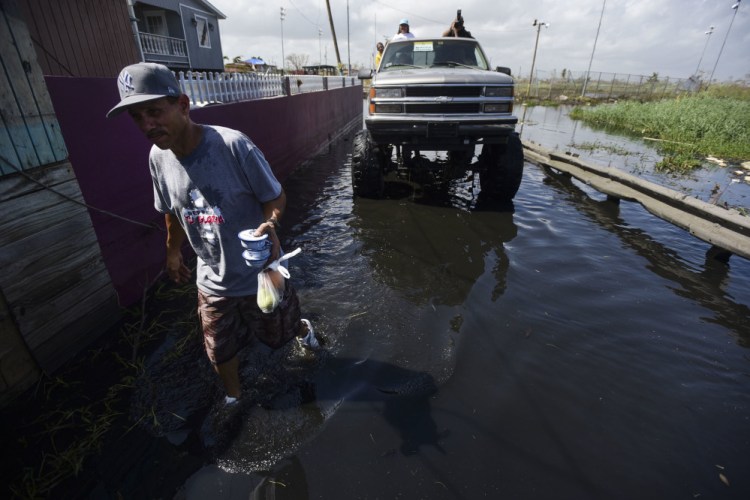 Amado Hernandez walks through a flooded area in Catano, Puerto Rico, on Thursday, carrying fruit and canned food one week after the passage of Hurricane Maria. The powerful storm has caused a near-total shutdown of the U.S. territory's economy that could last for weeks.