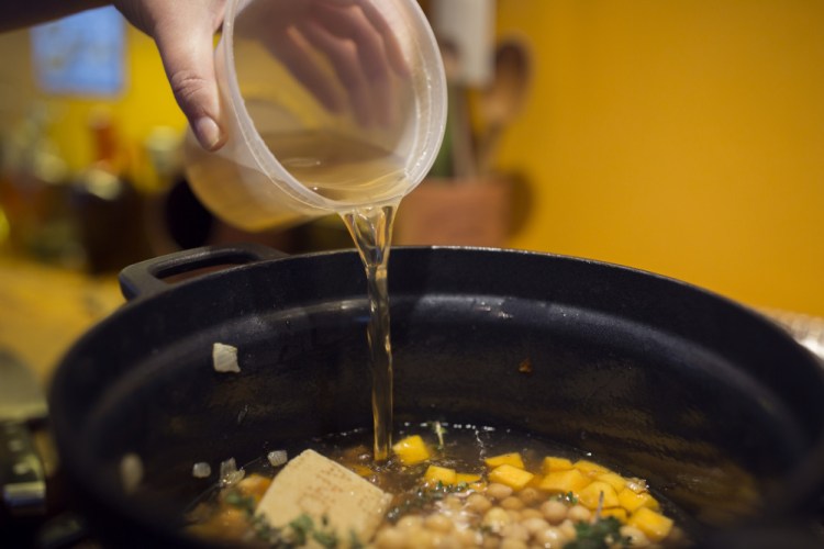 Christine Burns Rudalevige pours the broth into a mixture of chickpeas, butternut squash, Parmesan rinds, garlic and thyme.