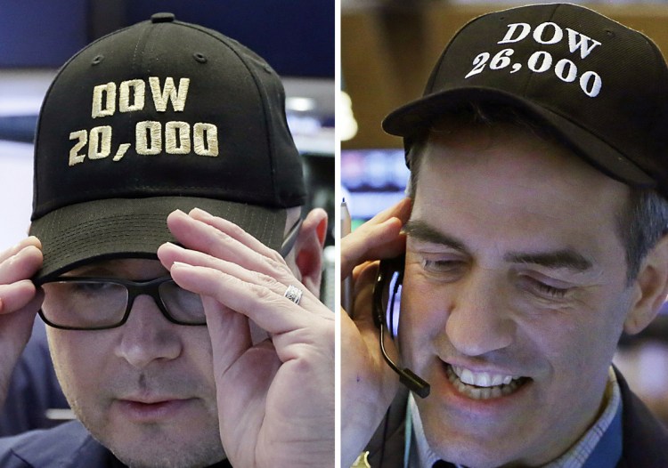 Specialist Mario Picone, left, adjusts his Dow 20,000 cap on Jan. 25, 2017, and trader Gregory Rowe wears a Dow 26,000 cap nearly a year later on Jan. 16, 2018, at the New York Stock Exchange.