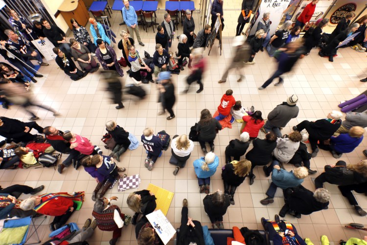 Wendy Schlotterbeck, center, of Auburn kneels with more than 100 fellow activists near the baggage claim at the Portland International Jetport on Saturday.