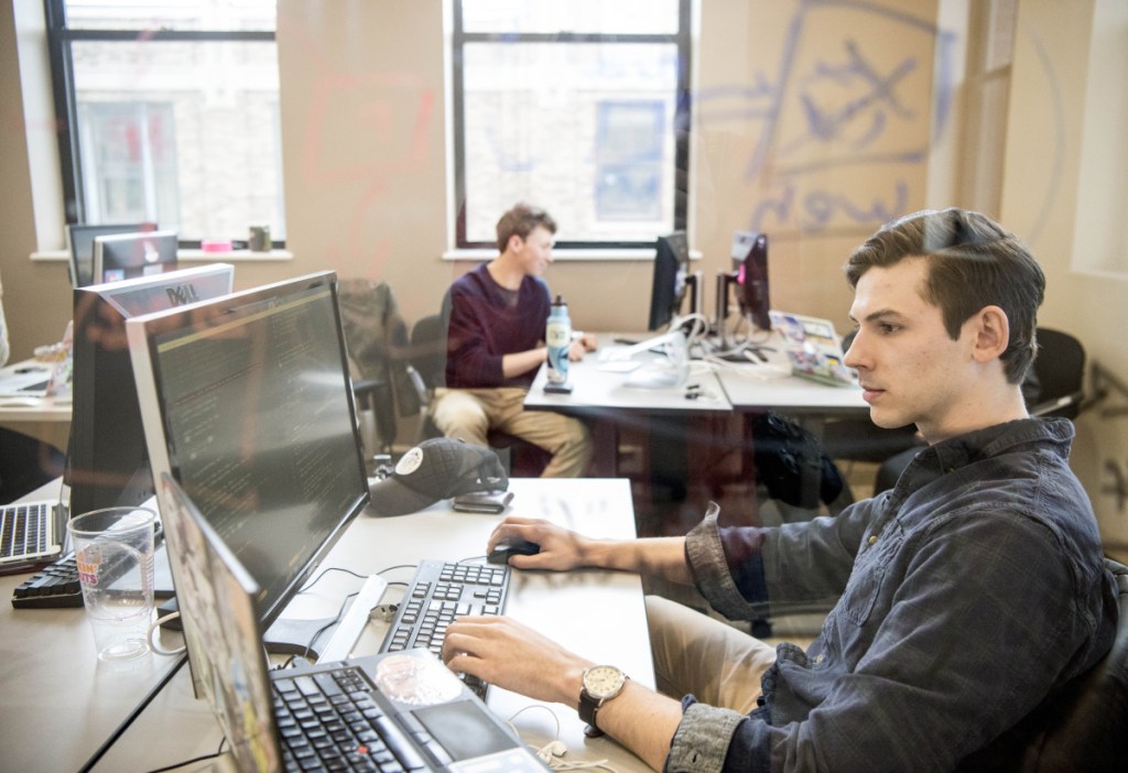 Colby College junior Walker Griggs, right, writes computer code Friday at Europiste, an outdoor retail company created by students, as the college continues efforts to revitalize downtown Waterville.