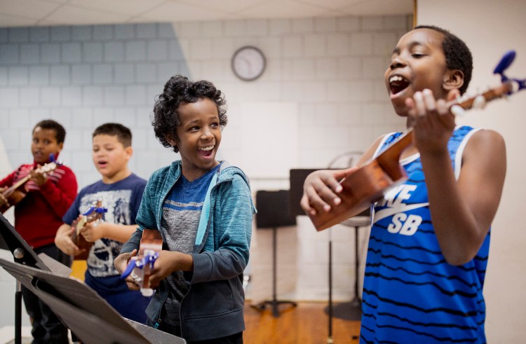 Khalid Mahmed, 11, center, and his classmate John Cubahiro, 9, practice on their brand new ukuleles before their performance at Riverton Elementary School. Lee Urban, the founder of the nonprofit Ukuleles Heal the World, gave all six of his vacation week camp students ukuleles to take home with them. Staff photo by Brianna Soukup