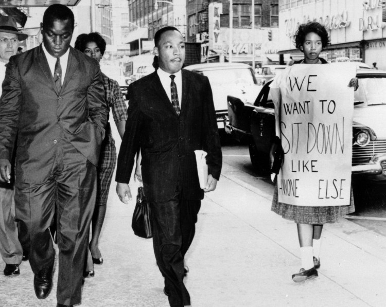 African Americans continue to struggle to attain economic, educational and social equality, decades after the far more successful efforts to end overt discrimination, such as the lunch counter sit-ins for which Martin Luther King Jr., center, was arrested by Atlanta Police Capt. R.E. Little, left rear, in October 1960. With the minister are Lonnie C. King (no relation), a college student and protest organizer; another student demonstrator, Marilyn Pryce, center rear, and an unidentified woman.