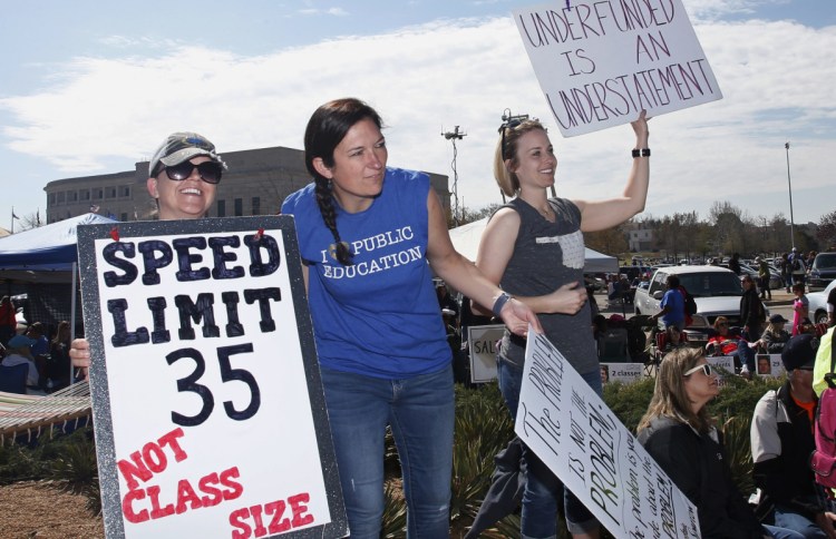 Teachers from Oolagah, Okla., Melinda Dale, from left, Scarlett Sellmeyer and Sierra Ryan, hold signs Tuesday at the Capitol in Oklahoma City as protests continue over school funding. After a day of teaching first-graders, Dale cleans the school.