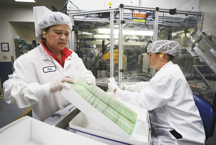 Production specialist Sea Neak, left, works with trainee Patricia Phillips as they batch product in boxes for quality-control testing last week at Abbott. 