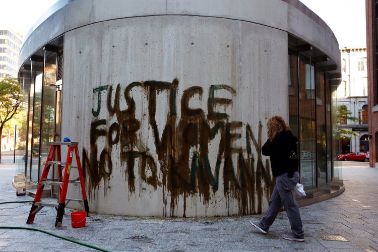 A woman, who declined to give her name, works to remove graffiti from a building near U.S. Sen. Susan Collins' downtown Portland office on Friday morning. 