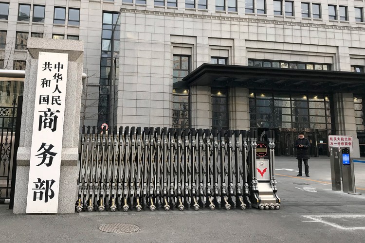 A man checks his mobile phone near the main entrance gate of the Ministry of Commerce in Beijing on Wednesday. U.S. and Chinese envoys extended trade talks into a third day Wednesday after President Trump said negotiations aimed at ending a tariff war were "going very well." 