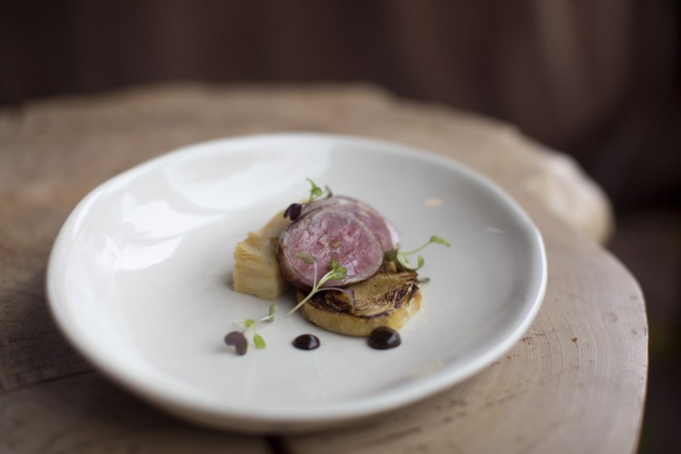 Bacon-wrapped lamb served with seared cabbage and a millefeuille of potato and celery root, black garlic puree and micro mustard greens at Hugo's.