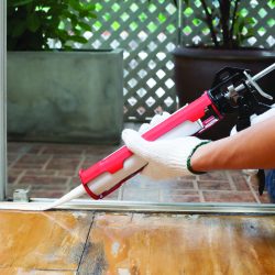 Image of a disembodied hand and arm using a caulking gun to seal a doorframe.