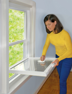 A woman cleans her windows from the inside of her home by tilting the sash inward.