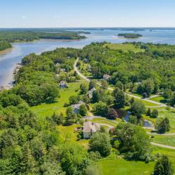 A peninsula covered in bright green grass and trees is surrounded by a river and then the open ocean